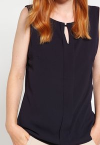 Top sin mangas de color navy con apertura en forma de llave en el frente y una textura suave. Presenta costuras mínimas y un corte relajado, diseñado para la comodidad.