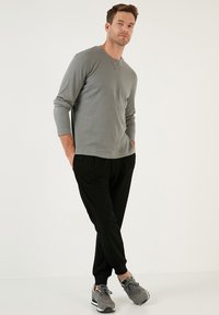 Szürke bordázott, hosszú ujjú póló fekete, laza szabású nadrággal és szürke sportcipővel párosítva. Kerek nyakkivágással és mandzsettákkal rendelkezik az ujjaknál.