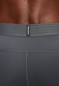Primer plano de la parte baja de la espalda y la cintura de una persona de piel oscura que lleva leggings deportivos Nike Pro de color gris oscuro con una banda elástica ancha.