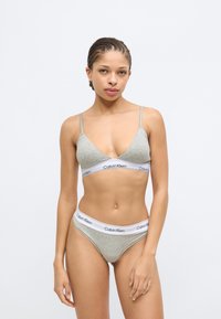 Απαλό γκρι βαμβακερό μπουστάκι και τόνγκα που ταιριάζουν, με λεπτές τιράντες και λευκή ζώνη μέσης με το λογότυπο "Calvin Klein". Ομαλή υφή, μινιμαλιστικός σχεδιασμός.