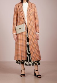 Pitkä ruudullinen takki oranssina ja valkoisena, käytetty mustan ja kermanvärisen kuviollisen hameen päällä. Varustettu kevyellä käsilaukulla ja mustilla remmitekijöillä.