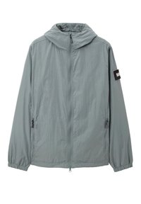 Giacca leggera con cappuccio in tessuto grigio tenue. Presenta una chiusura frontale a zip, polsini elasticizzati e tasche laterali con zip.