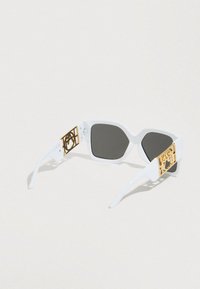 Λευκά γυαλιά ηλίου με γκρι φακούς, γωνιώδη σχήμα και ναούς με χρυσές λεπτομέρειες και περίπλοκο σχέδιο με ανοίγματα.