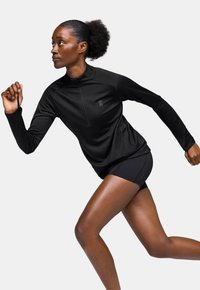 Haut de sport noir avec un design à demi-zip et des manches longues, associé à un short noir. Présente un petit logo sur la poitrine et une texture lisse.