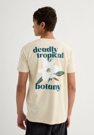 Camiseta de algodón color crema con un diseño gráfico floral y el texto "botánica tropical mortal" en tipografía en negrita de color teal y azul oscuro.