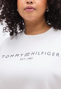 Ανοιχτό γκρι φούτερ από βαμβάκι, με το λογότυπο "TOMMY HILFIGER" σε μαύρο και το κείμενο "EST. 1985", στρογγυλή λαιμόκοψη και ριμπ μανσέτες.