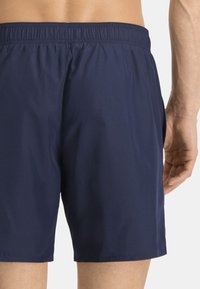Bañador azul marino confeccionado en tejido ligero, con una cinturilla elástica y un bolsillo lateral. Textura suave con un diseño sencillo.
