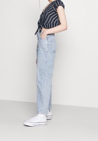 Jeans blu in denim a vita alta con gamba dritta, abbinati a un top corto a righe blu e bianche con nodo frontale, completati da sneakers bianche.