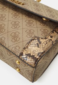 Brun monogrammeret håndtaske med guldstuds og en slangeskinnede tekstur i bunden af hjørnet mod en hvid baggrund.