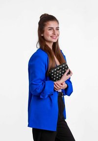 Černá taška na klíče s puntíky, kterou drží osoba oblečená v modrém oversized blejzru, vyrobená z hladké látky a obdélníkového tvaru.