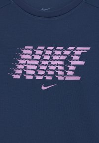 Tamno plava majica s teksturiranim ružičastim grafičkim prikazom "NIKE" u izobličenom stilu. Uključuje mali ružičasti Nike logo na dnu.