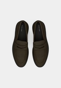 Mocassins vert foncé en tissu doux, avec un bout arrondi, des coutures discrètes et une bande texturée sur le dessus pour plus de détails.