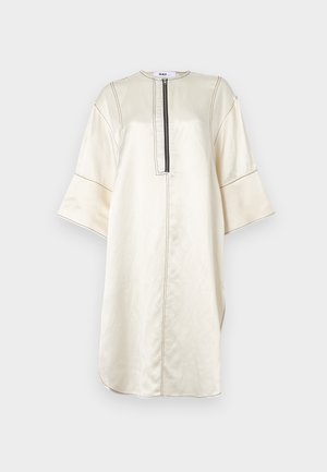 Beige tunika kjole laget av glatt stoff. Har en halvlang glidelås, vide ermer, splitt i siden og kontrasterende sømdetaljer.