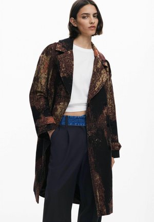 Cappotto lungo nero con un motivo testurizzato multicolore nelle tonalità di marrone e oro. Presenta ampi rever e dettagli con bottoni. Abbinato a una parte superiore bianca e una cintura blu.