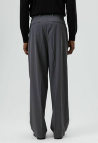Pantalon large gris en tissu lisse, avec deux poches arrière, design plissé et taille ajustée.