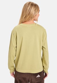 Camicia verde a maniche lunghe realizzata in tessuto morbido, con vestibilità rilassata, scollatura rotonda e dettagli di cucitura visibili.