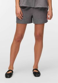 Shorts grises con una tela texturizada, de longitud media a los muslos, con un corte recto y detalles cosidos. Combinados con zapatos planos negros.