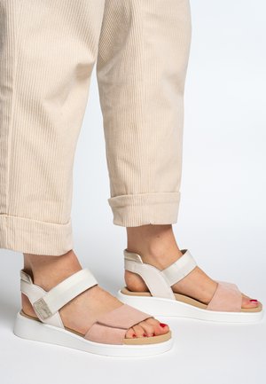 Lightweight sandals with a pink suede and white synthetic upper, featuring a Velcro strap and a thick white sole. Worn with beige corduroy pants.