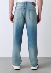 Világoskék farmernadrág, amely fokozatos mosási hatással, egyenes lábú kialakítással, öt zsebbel és egy kis márkafogóval rendelkezik a derékon.