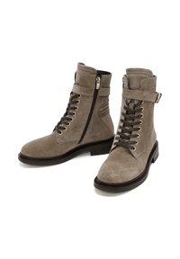 Bottes chelsea en daim gris avec un bout rond, un laçage sur le devant, une fermeture éclair sur le côté et un accent de sangle à la cheville. Semelle plate en caoutchouc.
