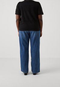 Top de ganchillo negro con un patrón texturizado, combinado con unos jeans de mezclilla azul de tiro alto. Los jeans tienen un corte holgado y un ligero desgaste.