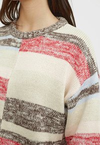 Maglione lavorato a maglia con scollo rotondo, caratterizzato da strisce orizzontali in rosso, rosa, blu e marrone su uno sfondo crema. Dettaglio in filato testurizzato.