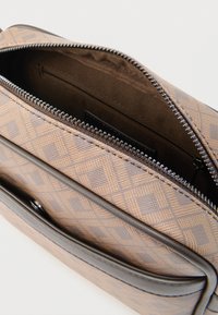 Καφέ τσάντα χειρός με γεωμετρικό σχέδιο, κλείσιμο με φερμουάρ, λείες δερμάτινες λεπτομέρειες και μαλακή, επενδεδυμένη εσωτερική επιφάνεια.