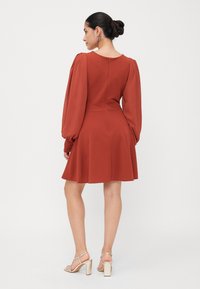 Röd miniklänning med puffiga långa ärmar, figursydd bodice och utsvängd kjol. Har en rund halsringning och dragkedja bak. Bärs med remsandaler.