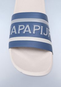 Sininen kumisaapasliuku sandalilla, jossa on teksturoitu valkoinen pohja, rohkea kohotettu logo ja vaakasuorat harmaat raidat remmissä.