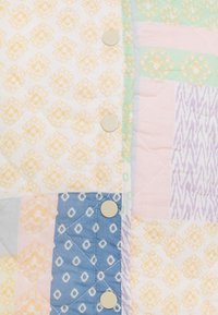 Colcha multicolor con patrones geométricos en tonos pastel de amarillo, verde menta, rosa y lavanda, con textura acolchada y botones redondos.