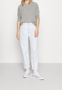 Ljusblå denimjeans med hög midja och avslappnad passform, i kombination med en strukturerad grå långärmad topp och vita högskaftade sneakers.