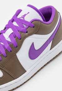 Gros plan d'une basket basse en cuir blanc et marron, avec le logo Nike violet, des lacets et une doublure intérieure violette.