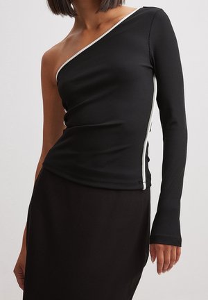 Donna che indossa un top nero a coste monospalla con una manica lunga e bordi bianchi, abbinato a una gonna nera.