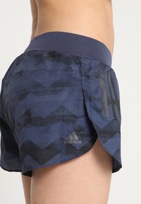 Pantalones cortos deportivos de color azul marino con un patrón texturizado, que presentan una amplia cinturilla elástica y tres rayas negras verticales en el costado.