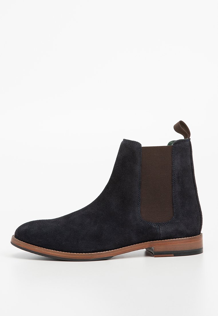 Schwarze Wildleder Chelsea-Boots mit elastischen seitlichen Einsätzen, runder Zehenform und brauner Gummisohle. Mit einer Zuglasche hinten für ein einfaches Anziehen.