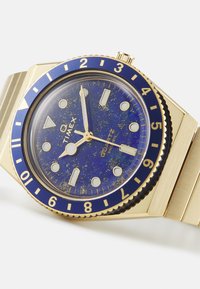 Montre à quartz Timex avec un boîtier et un bracelet en acier inoxydable doré. Le cadran bleu présente des accents dorés, des marqueurs d'heure et une lunette tournante.