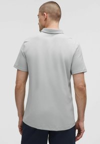 Grijze polo met korte mouwen, platte kraag en een gladde textuur. De achterkant heeft een klein naaddetail en is ontworpen voor een relaxte pasvorm.