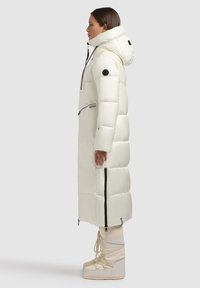 Piumino bianco con design trapuntato, colletto alto e tasche con zip. Abbinato a stivali beige con lacci e suole rialzate.