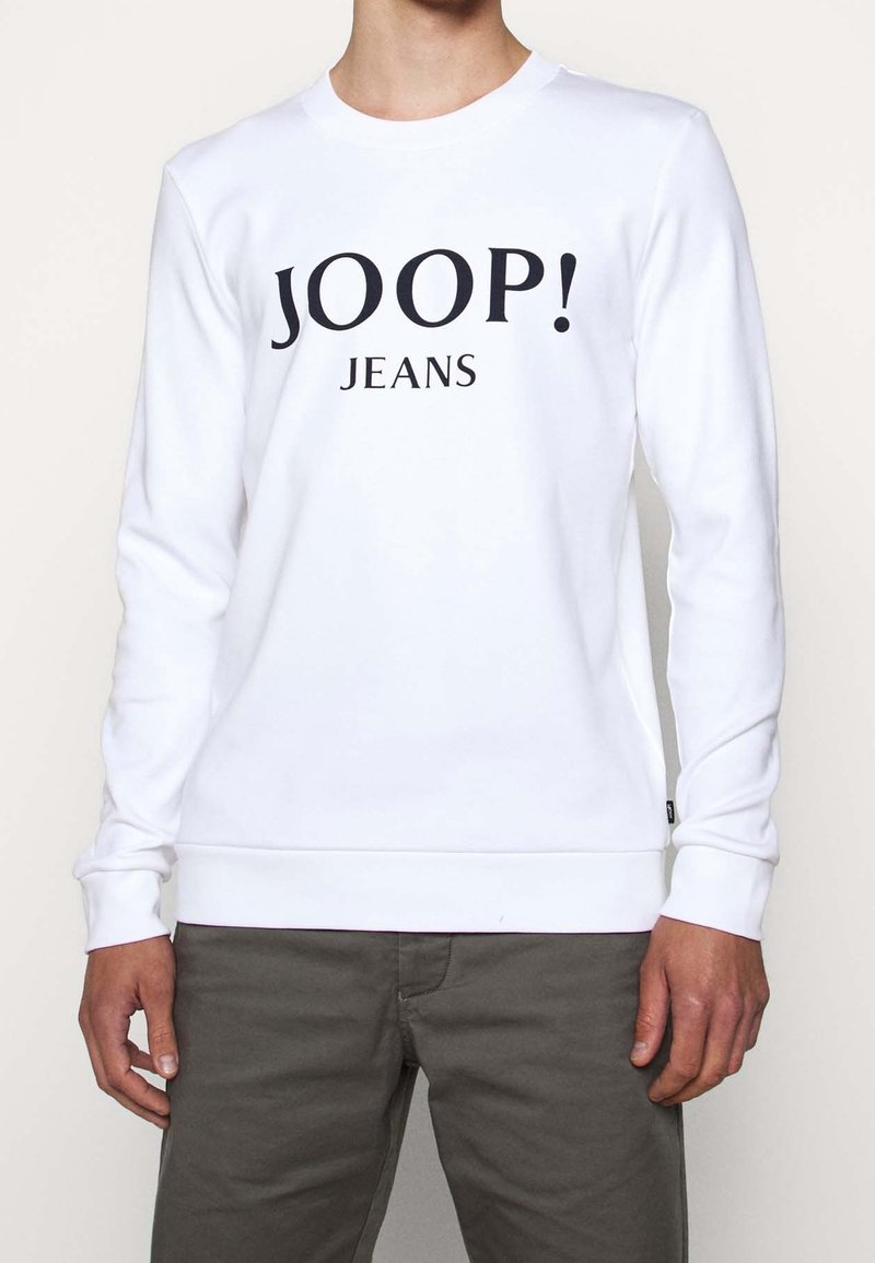 Sweatshirt blanc à manches longues avec le texte "JOOP! JEANS" en noir sur la poitrine. Design simple avec poignets et bord côte côtelés.