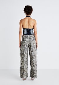 Haut en denim à col halter associé à un pantalon large en imprimé léopard. Détails en tissu transparent visibles sur le pantalon. Motifs texturés sur l'ensemble.