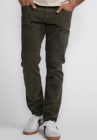 Olijfgroene ribfluweel broek met een rechte pijp, voorzien van voorzakken, gedragen met witte sneakers. Gelaagd stof, casual stijl.