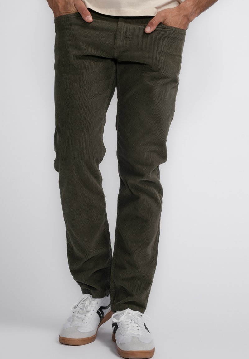 Olijfgroene ribfluweel broek met een rechte pijp, voorzien van voorzakken, gedragen met witte sneakers. Gelaagd stof, casual stijl.