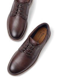 Paire de chaussures habillées marron en cuir à lacets avec bouts arrondis, coutures visibles et semelles intérieures marquées sur fond blanc.