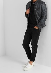 Svart skinnmotorcykeljacka med texturerade axlar, kombinerad med en svart t-shirt och uppvikta svarta jeans, avslutad med vita sneakers.