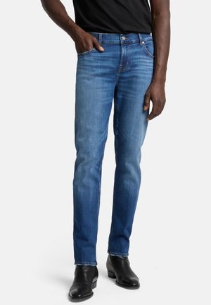 Blue denim jeans with a straight-leg cut, featuring a medium wash, copper stitching, and five pockets. Worn with black ankle boots.