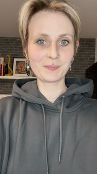 Gray hoodie with drawstrings, featuring a kangaroo pocket. The fabric appears soft. Accessories include earrings and a nose ring.