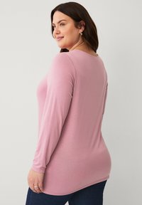 Long-sleeve pink top made from soft fabric, featuring a round neckline and a fitted silhouette, paired with dark blue jeans.