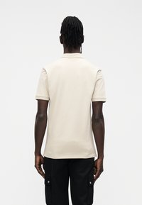 Polo beige in cotone, con collo classico, maniche corte e texture liscia. Indossata con pantaloni cargo neri.