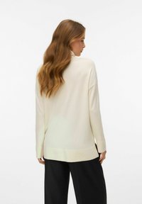 Kremowy sweter z półgolfem, długimi rękawami i luźnym krojem. Posiada gładką strukturę i nieco dłuższy tylny brzeg.