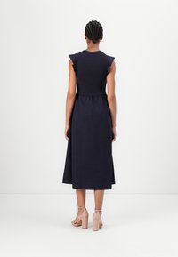 Navyblaues Midi-Kleid aus weichem Stoff, mit kurzen Rüscheärmeln und einem gerafften Taillenbereich, mit einem fließenden Rock. Kombiniert mit beigen Blockabsätzen.